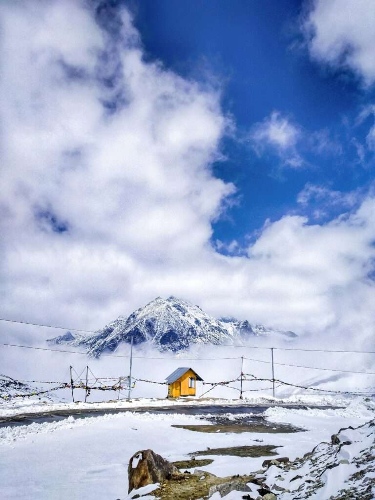 Tranquil mountain landscape featuring a yellow hut amidst snow and clouds. Ideal for winter scenery lovers.