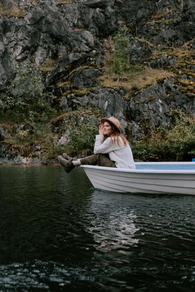 Young woman in a hat sits on a boat, enjoying a calm lake amid rocky surroundings.
