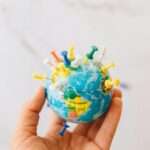 Close-up of a hand holding a mini globe with colorful push pins on a white background.